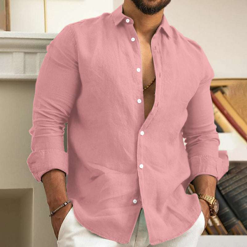 Man wearing a pink button-up shirt with rolled-up sleeves indoors.