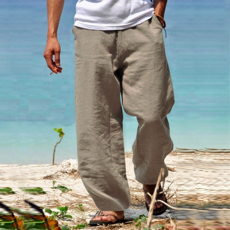 Person wearing beige wide-leg pants standing on a beach with clear blue water in the background.
