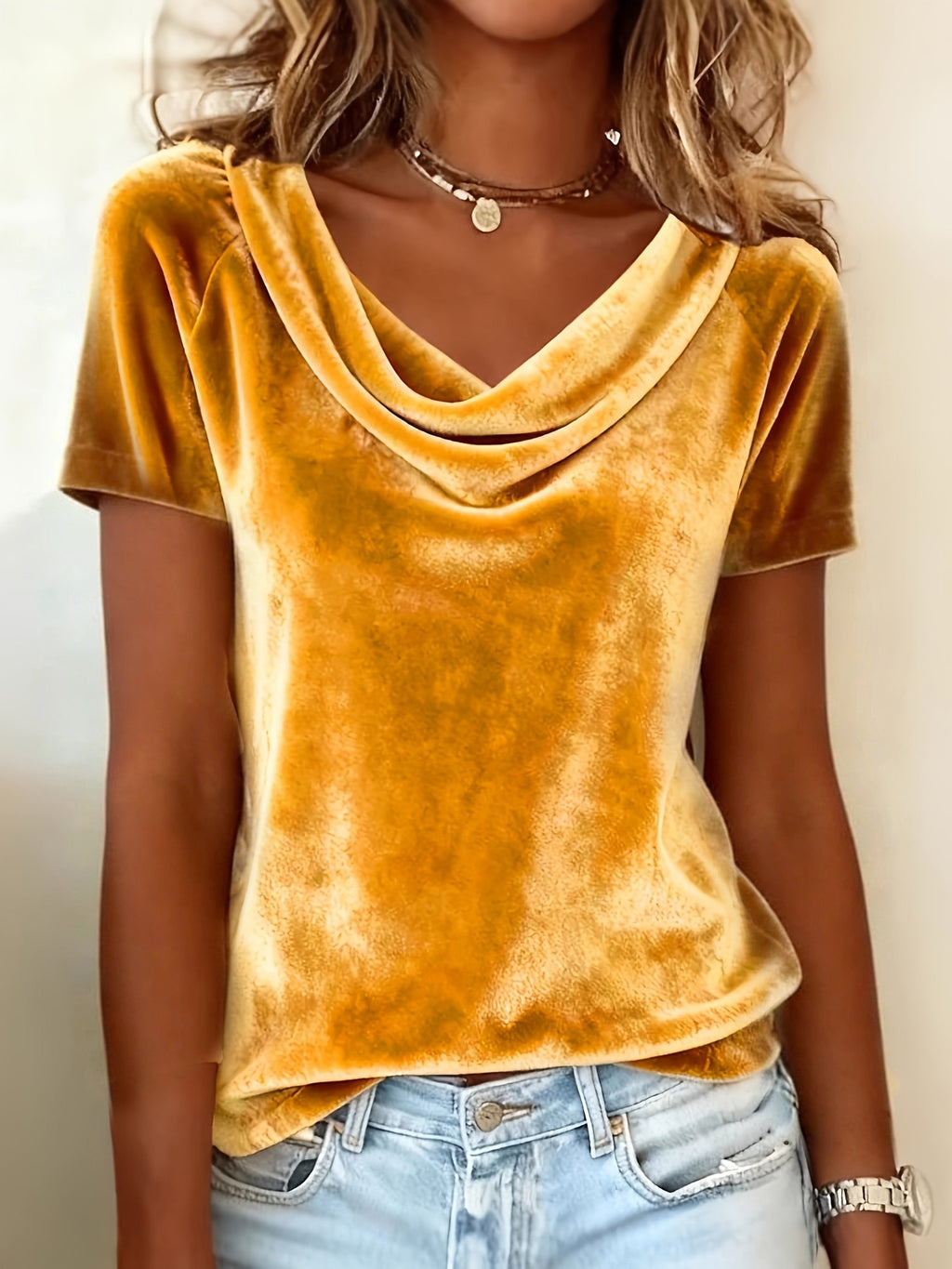 Person wearing a mustard yellow velvet top and light blue jeans against a neutral background