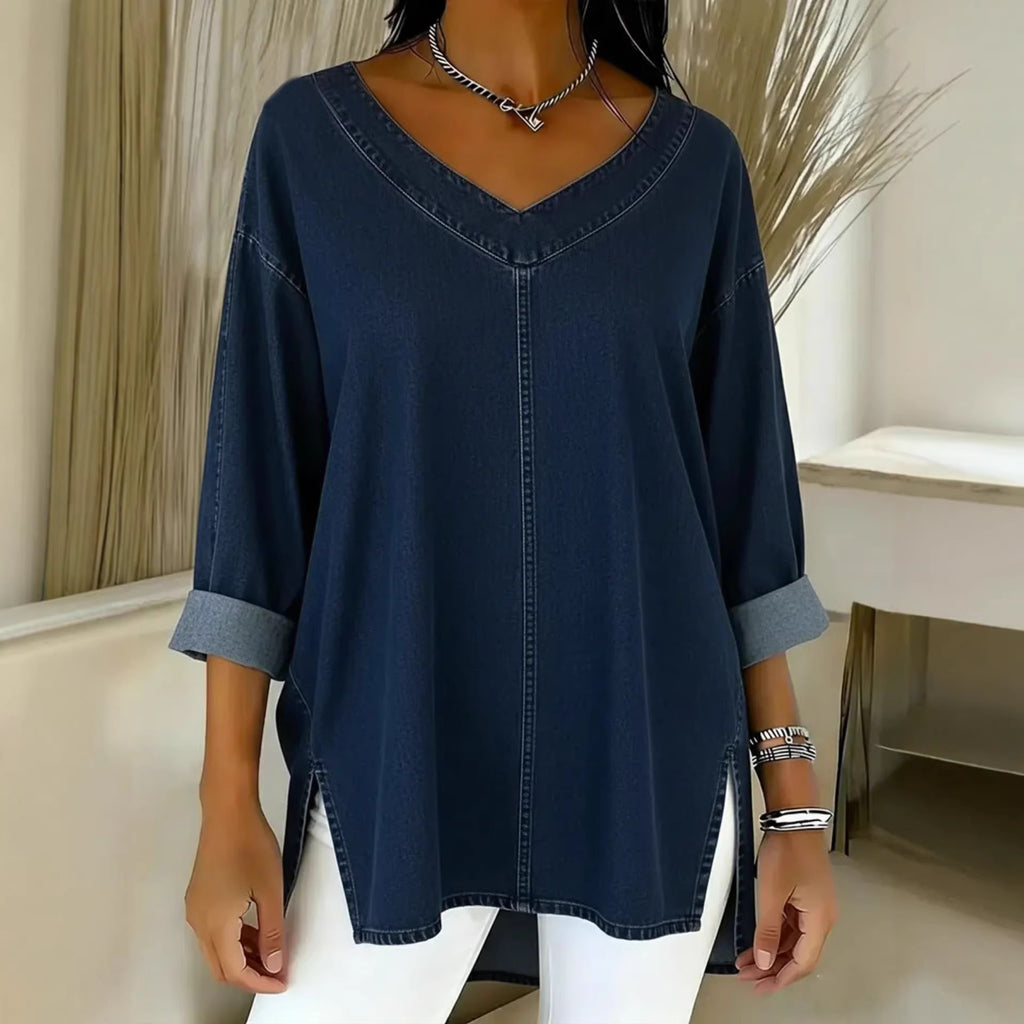 Person wearing a navy blue denim shirt with rolled-up sleeves in a minimalistic room.