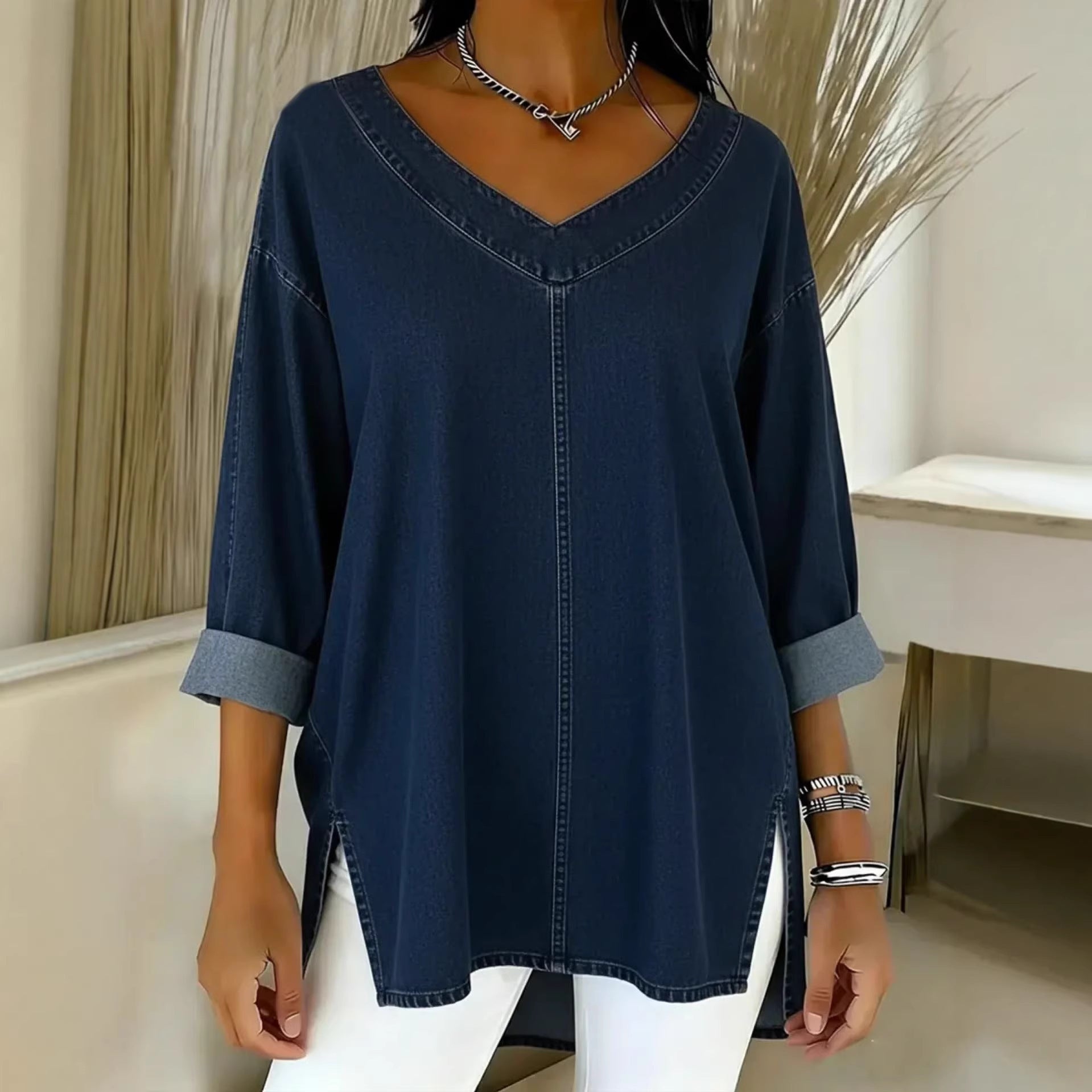 Person wearing a navy blue denim shirt with rolled-up sleeves in a minimalistic room.
