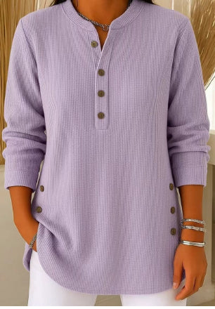 Person wearing a purple ribbed sweater with buttons, standing against a neutral background.