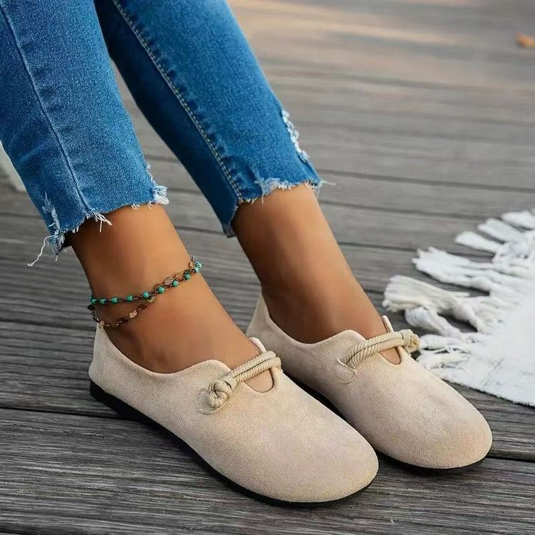 Beige loafers worn with blue jeans on a wooden floor.