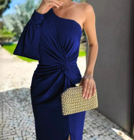Woman in a blue one-shoulder dress holding a gold clutch outdoors.