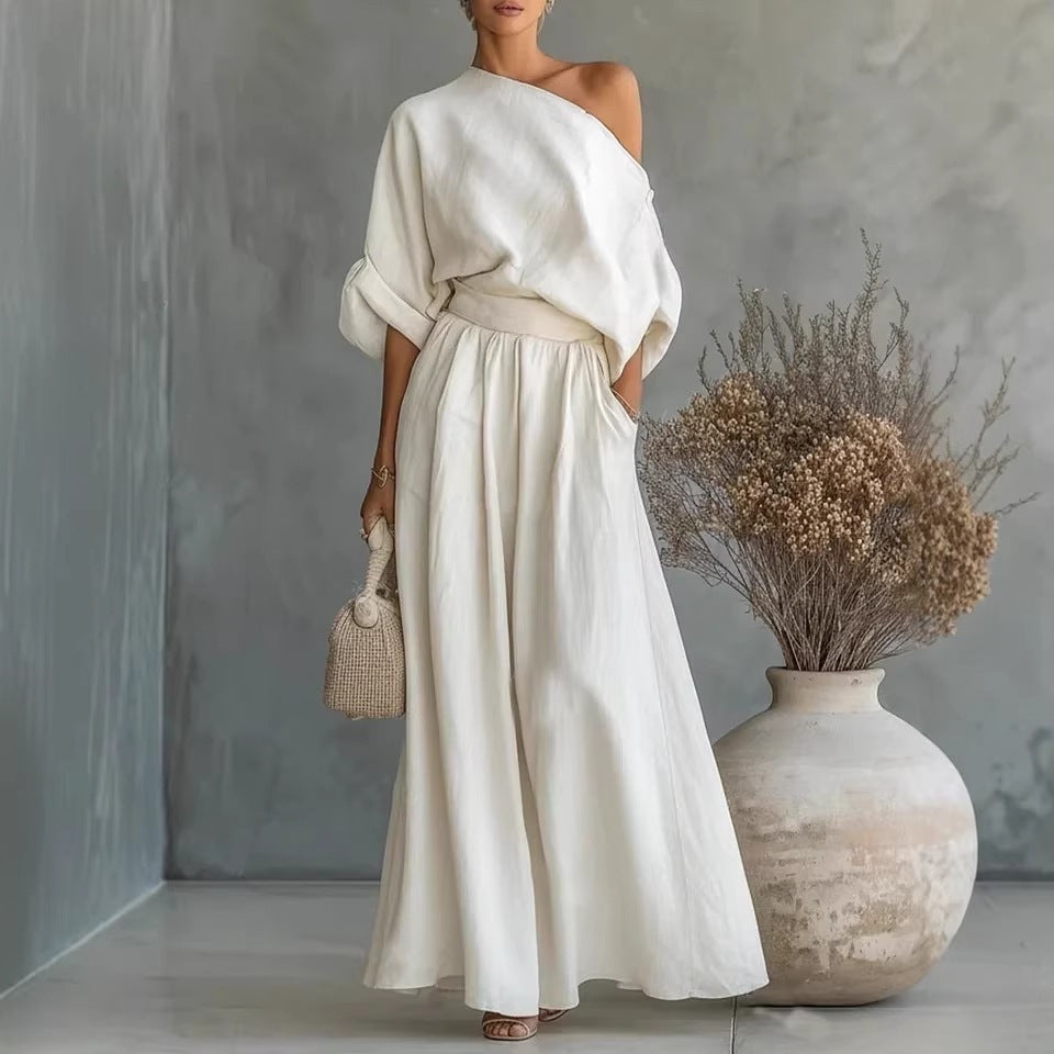 Woman in a white outfit standing next to a textured wall and decorative vase.