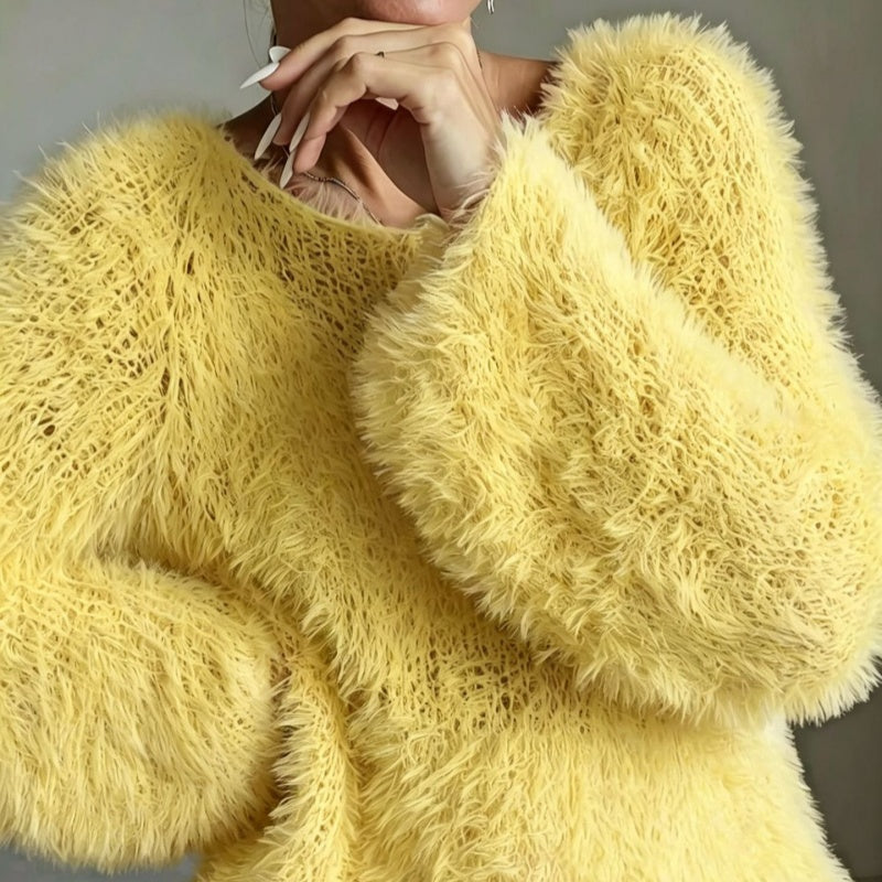 A close-up of a person wearing a fuzzy, oversized pale yellow knit sweater. The image is cropped to show the textured garment and part of the model's hands and chin against a plain gray background.