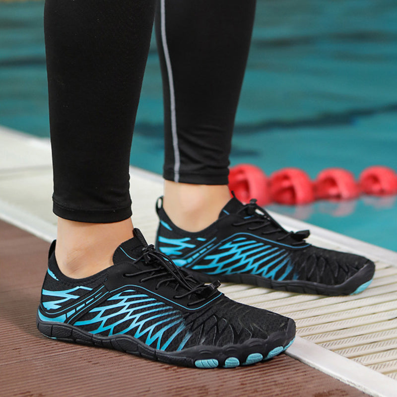 Black and blue athletic shoes worn by a person standing on a pool deck with red pool noodles in the background.