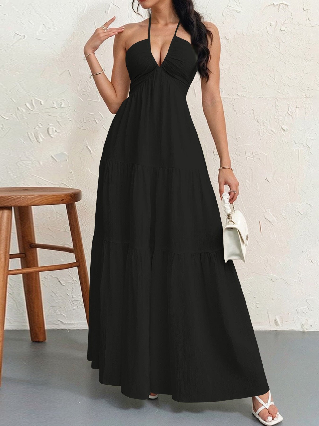 Woman wearing a black halter neck dress against a white wall.