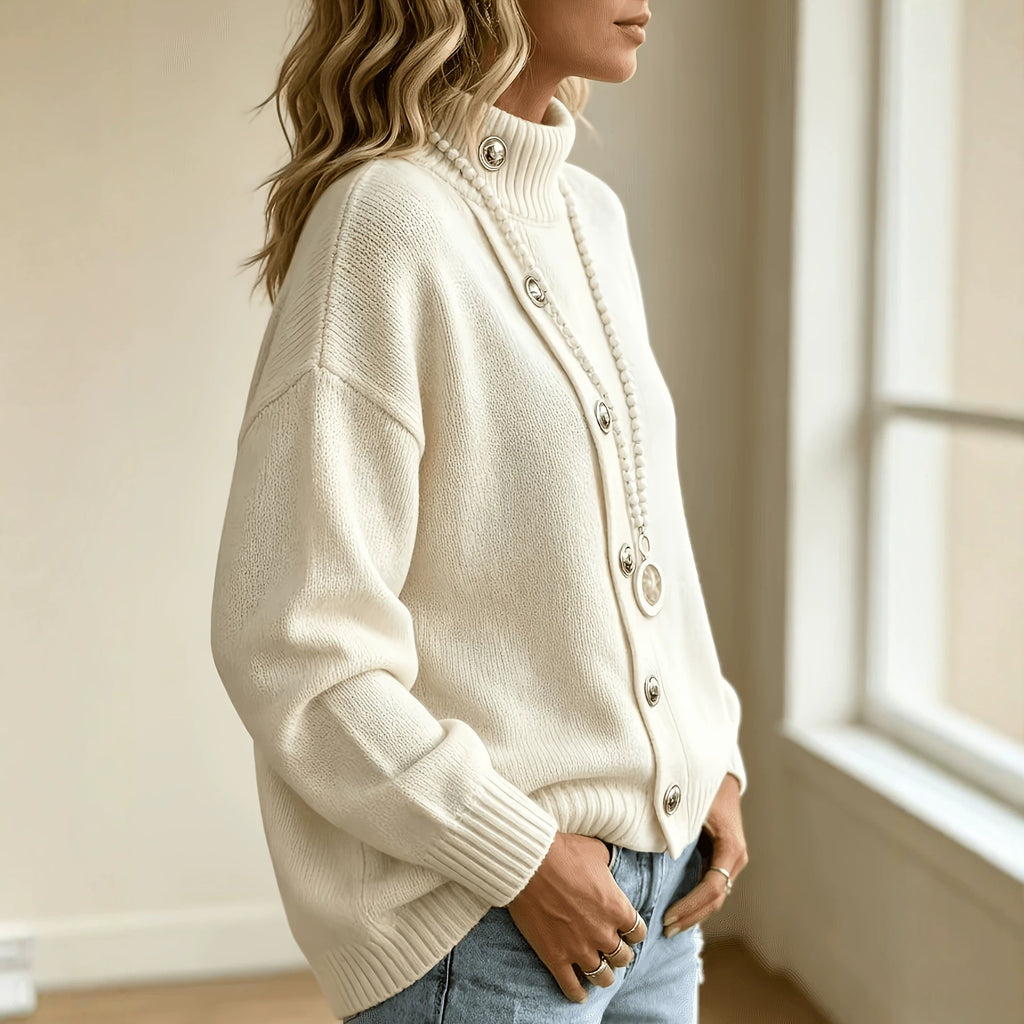 A woman wearing a cream-colored ribbed knit cardigan sweater with silver-tone buttons, paired with light-wash blue jeans, standing in a brightly lit room.