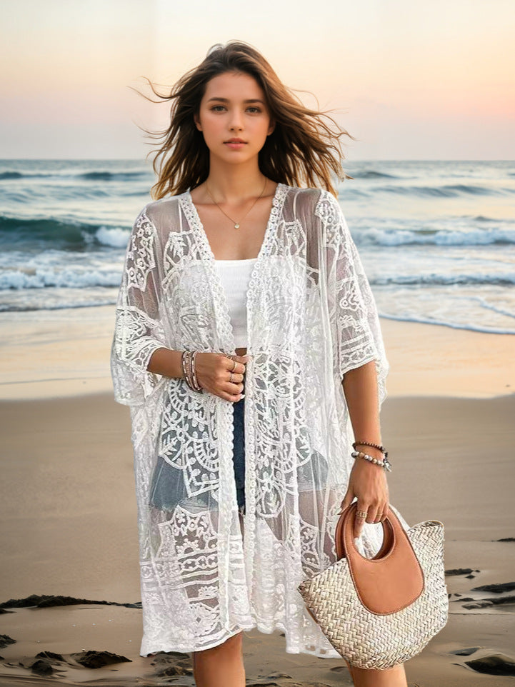 Woman in a white lace cover-up standing on a beach with ocean waves in the background