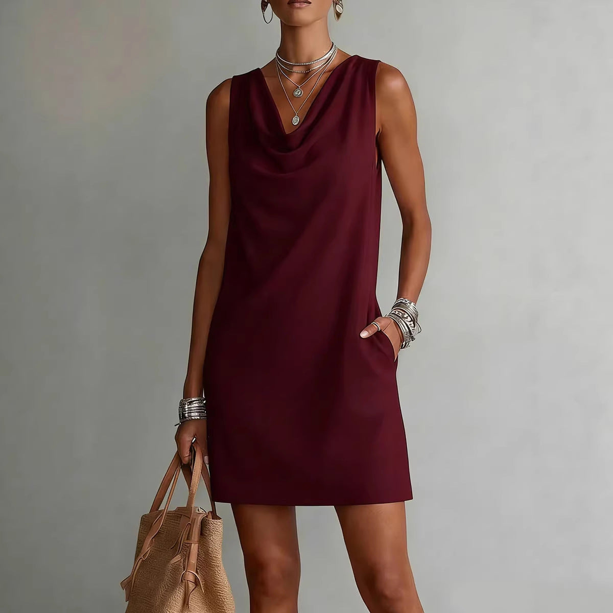 Woman wearing a burgundy dress holding a beige handbag against a gray background