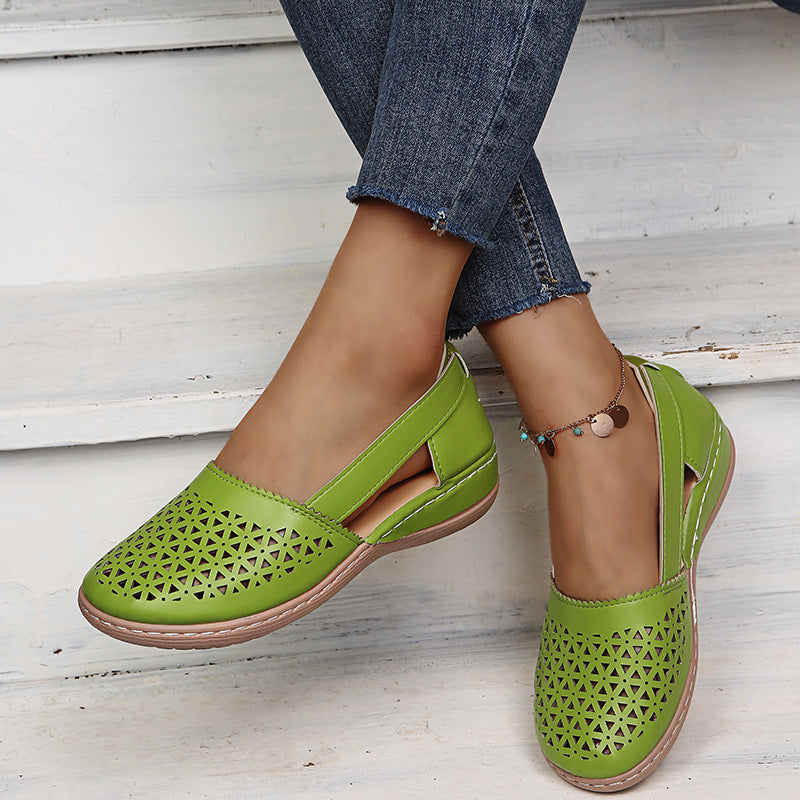 Green flat shoes with cut-out design worn with blue jeans on a light wooden floor.
