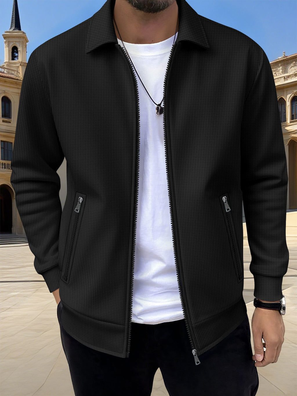 Person wearing a black textured jacket over a white shirt with a blurred architectural background