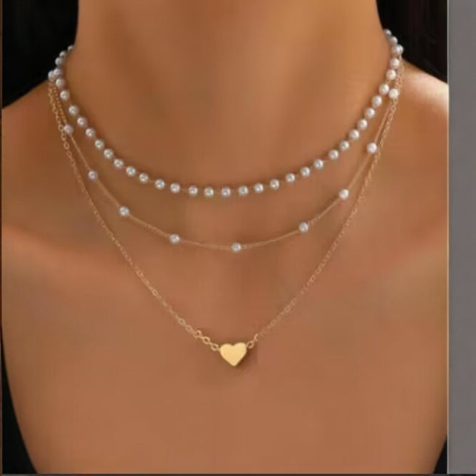Two pearl necklaces and a gold necklace with a heart pendant on a mannequin.