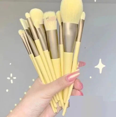 Hand holding a set of yellow makeup brushes with gold ferrules, ideal for beauty routines