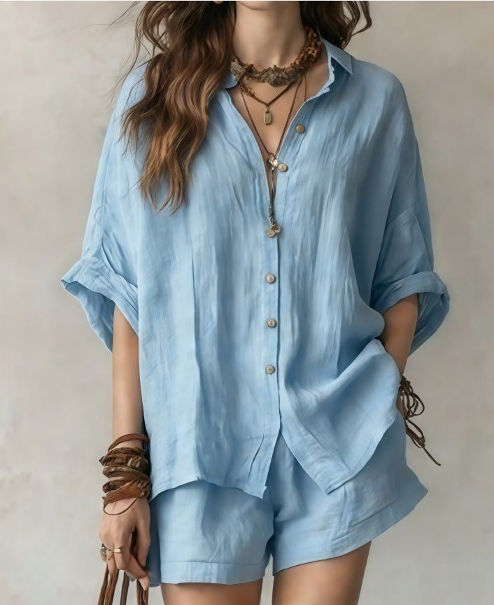 Person wearing a light blue shirt and shorts set with accessories on a neutral background