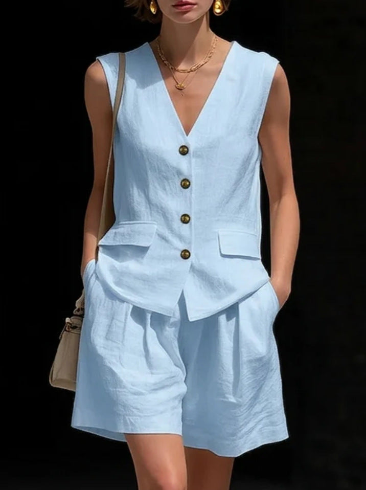 Woman wearing a light blue sleeveless top and shorts set with gold buttons on a black background.