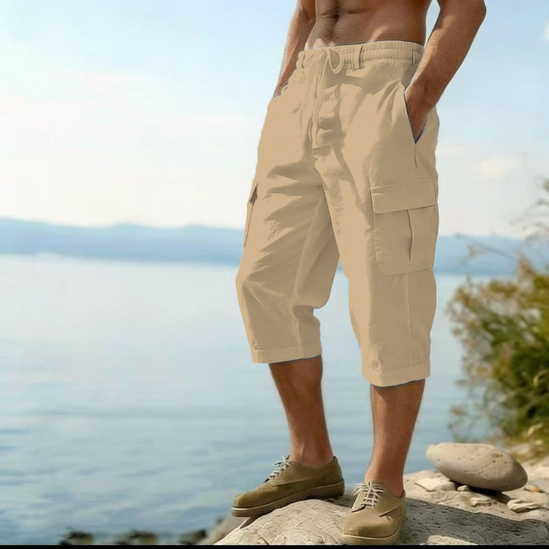 Person wearing beige cargo shorts standing by a body of water with mountains in the background.