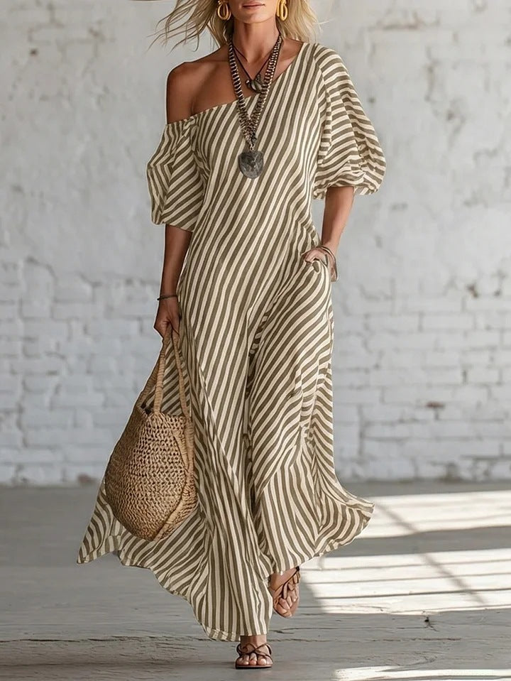 Woman wearing a striped dress with a woven bag against a white brick wall.