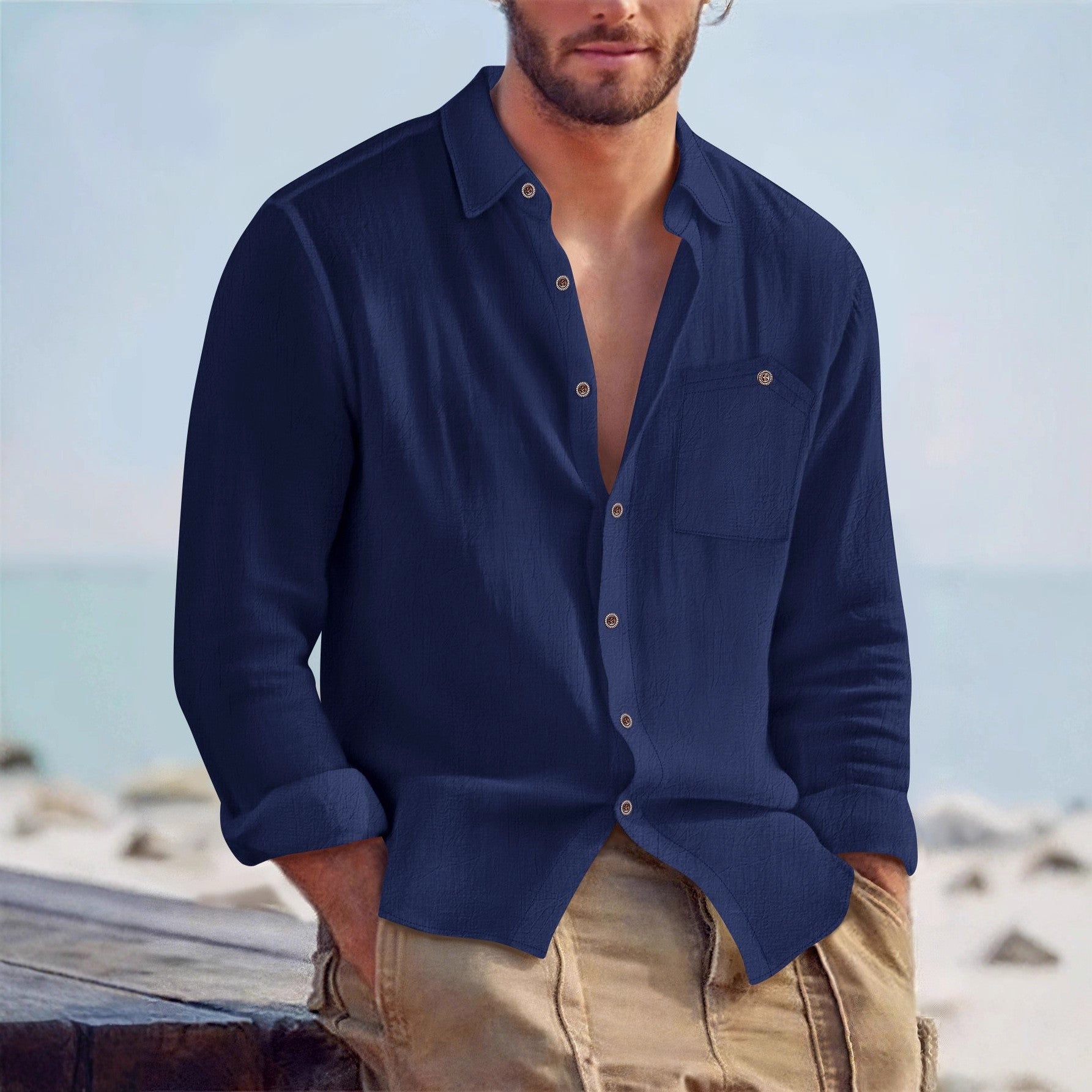 Man wearing a navy blue shirt with rolled-up sleeves and beige pants against a beach background
