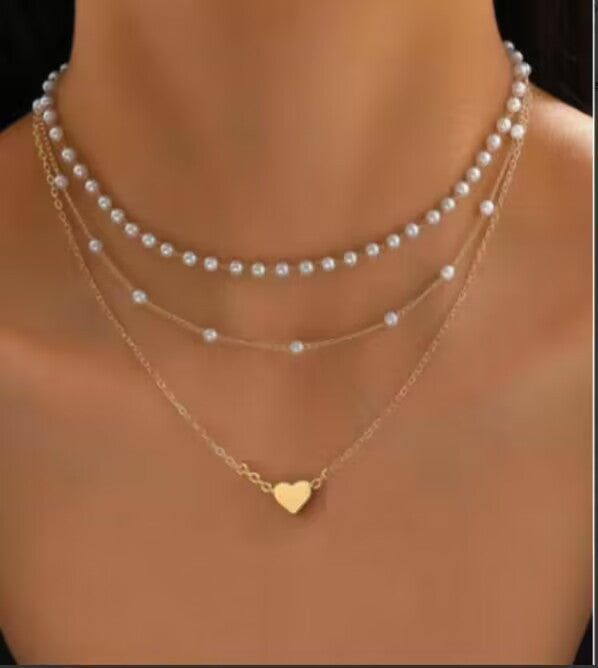 Two pearl necklaces and a gold necklace with a heart pendant on a blurred background
