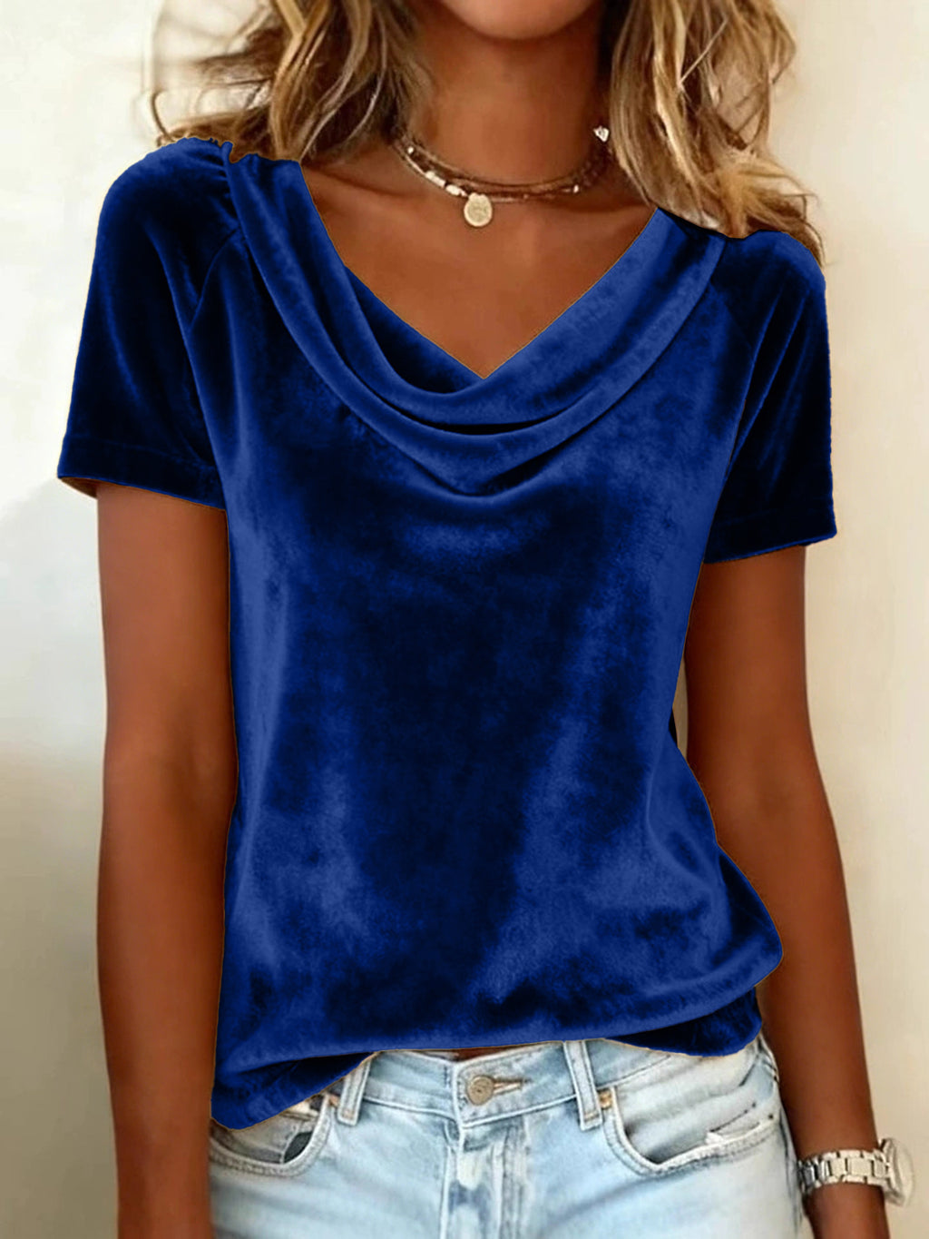 Person wearing a blue velvet top and light blue jeans against a neutral background
