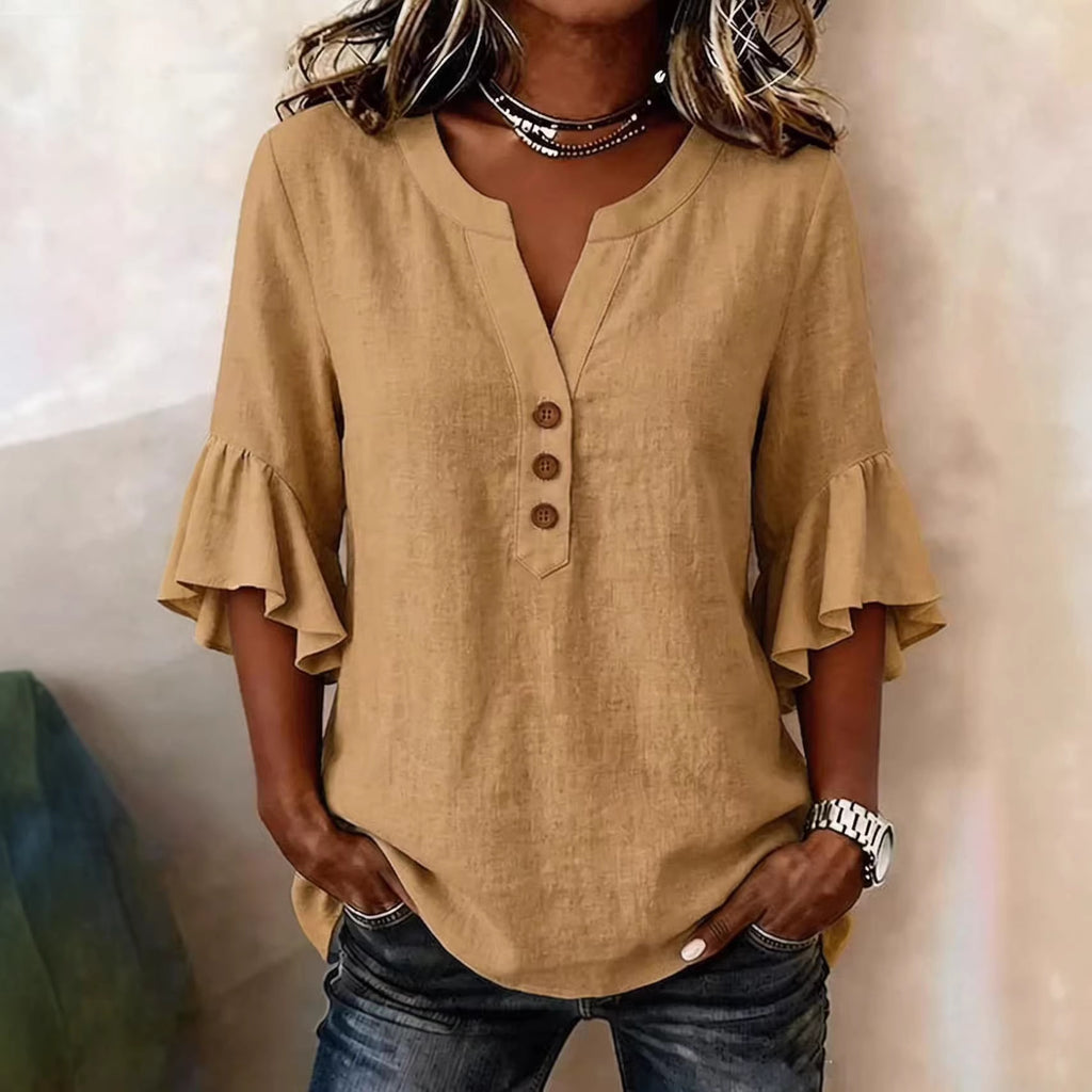 Person wearing a beige blouse with ruffled sleeves against a neutral background