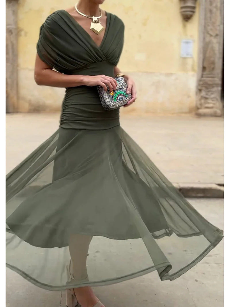 Woman in a green dress holding a patterned clutch in an outdoor setting