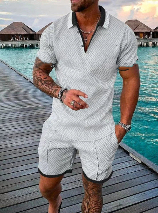 Man in a white patterned outfit standing on a wooden dock with water and huts in the background