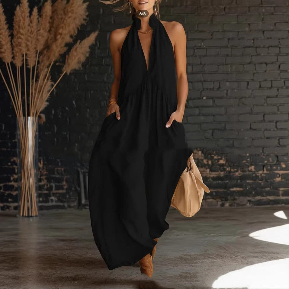 Woman wearing a black dress with a beige bag against a black brick wall.
