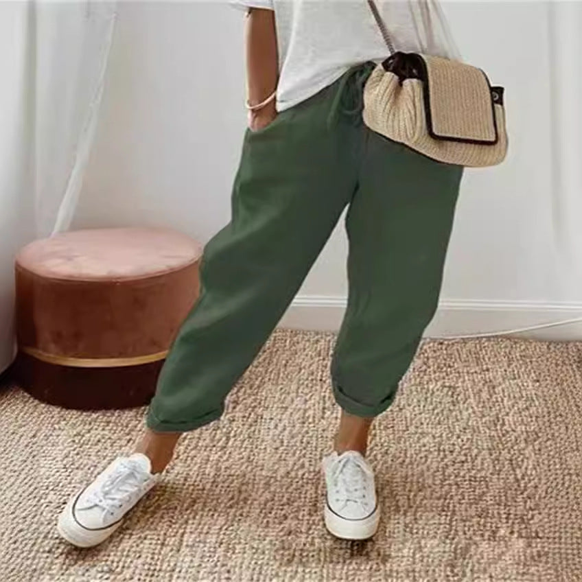 Person wearing green pants and white sneakers with a beige bag, standing on a carpeted floor.