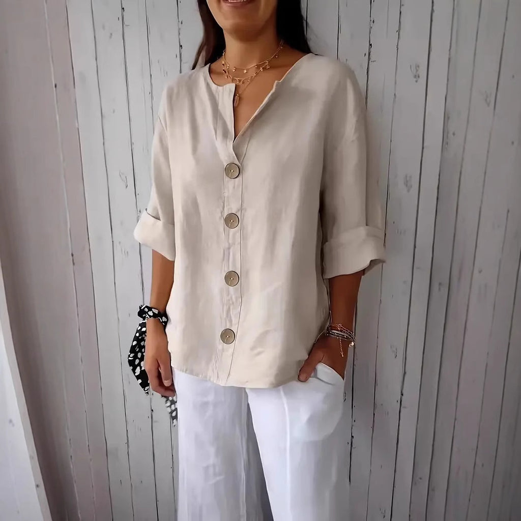 Woman wearing a beige button-up shirt and white pants against a wooden paneled wall.