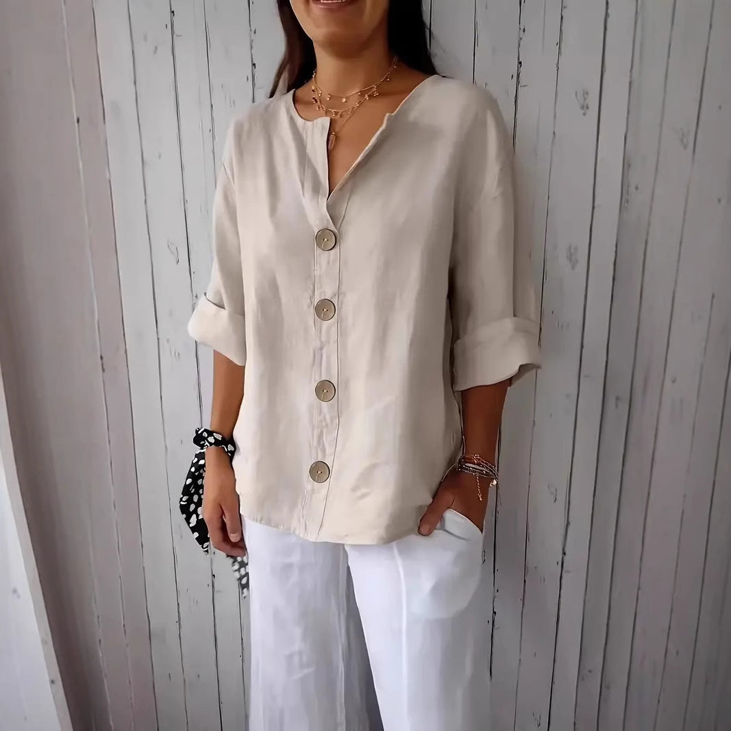 Woman wearing a beige button-up shirt and white pants against a wooden paneled wall.