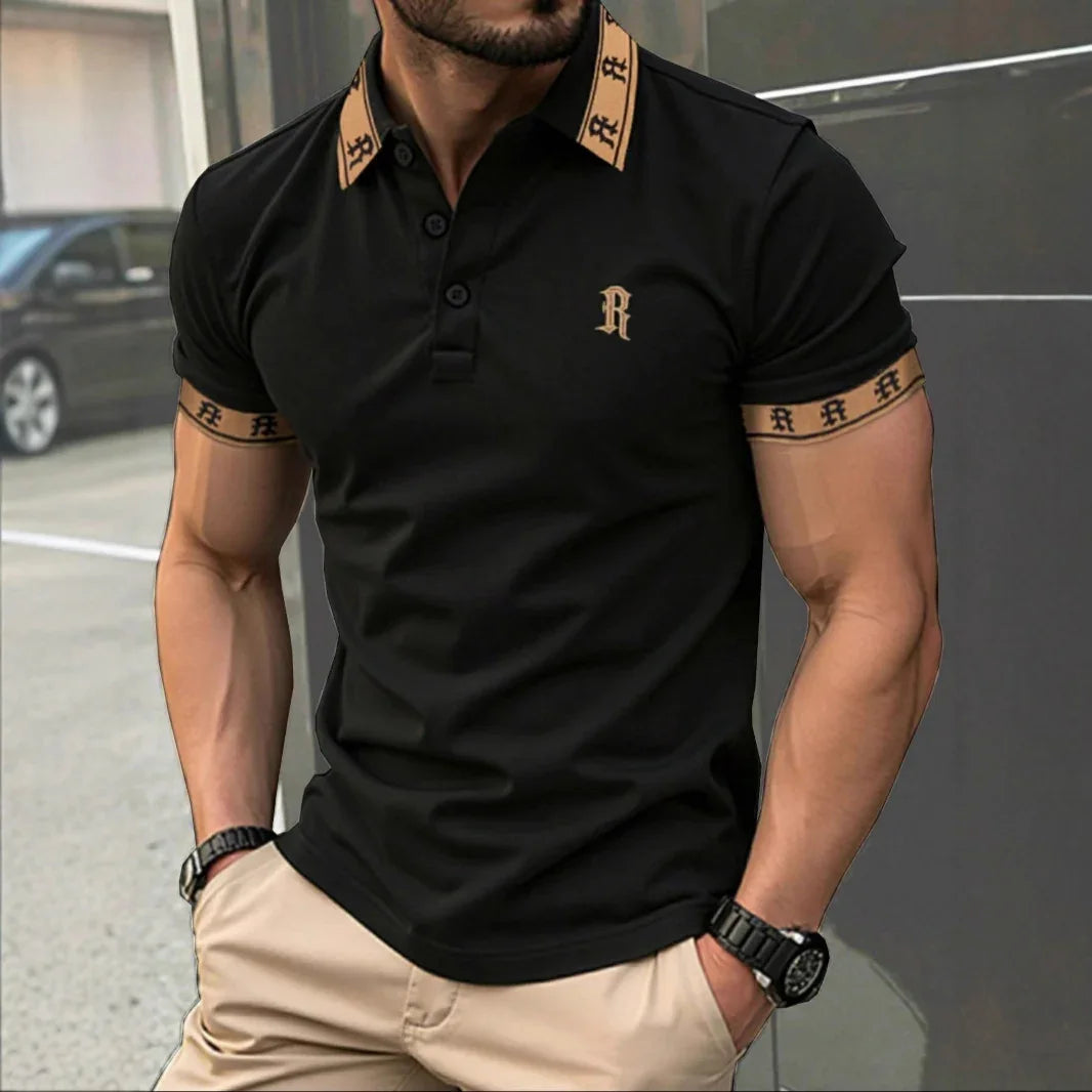 Man wearing a black polo shirt with gold accents and a logo, standing outdoors.