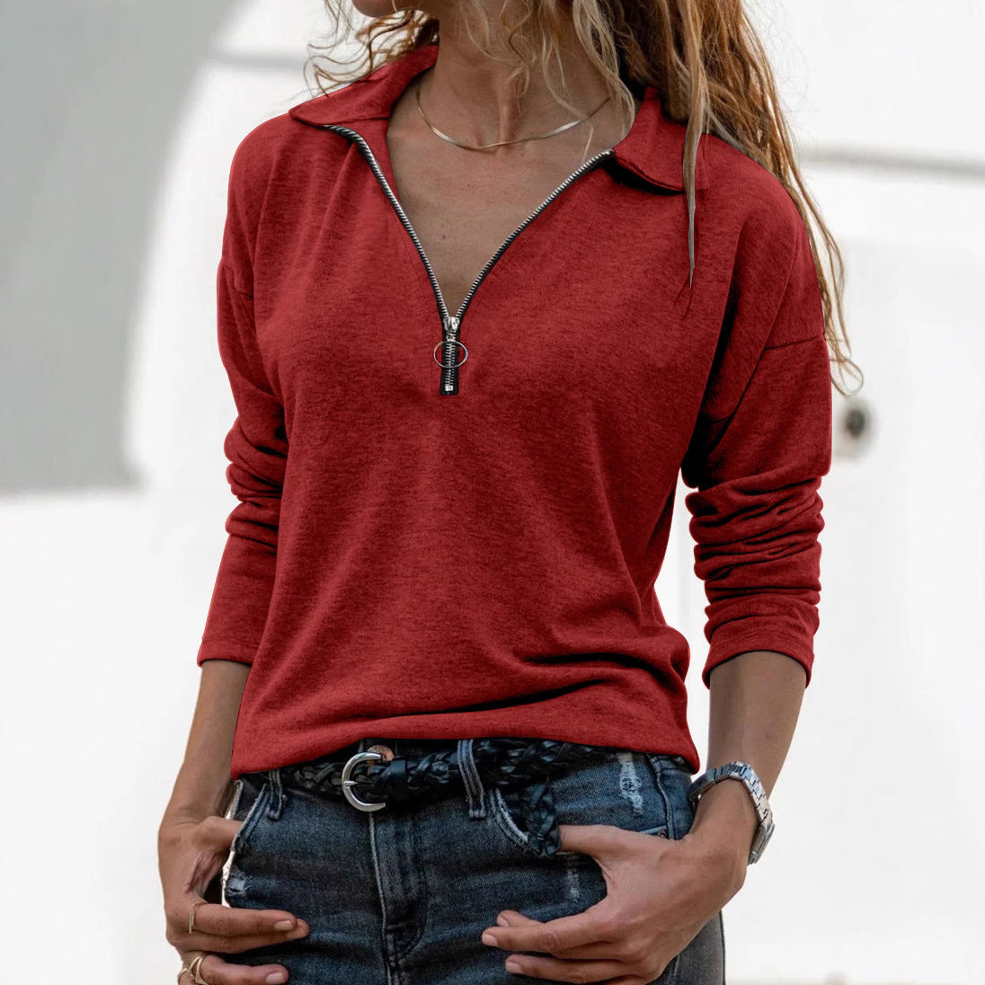 Person wearing a red long-sleeve top with a zipper detail, standing against a neutral background.
