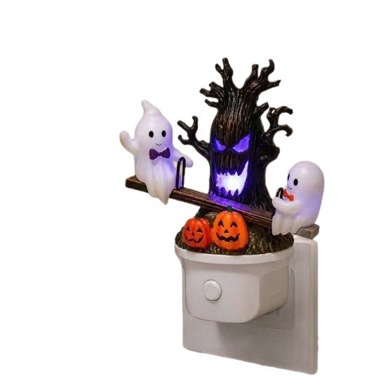 Halloween night light plug-in featuring a spooky tree with glowing purple eyes, two white ghosts, and three orange jack-o'-lantern pumpkins on a white electrical outlet insert.