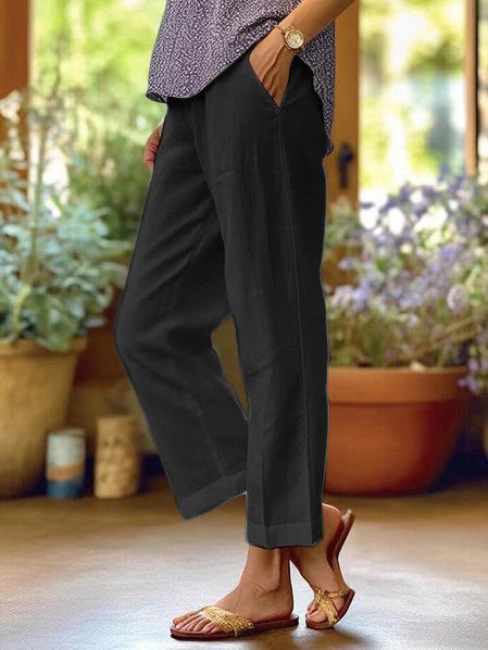 Person wearing black pants and a patterned top in a home setting with plants.