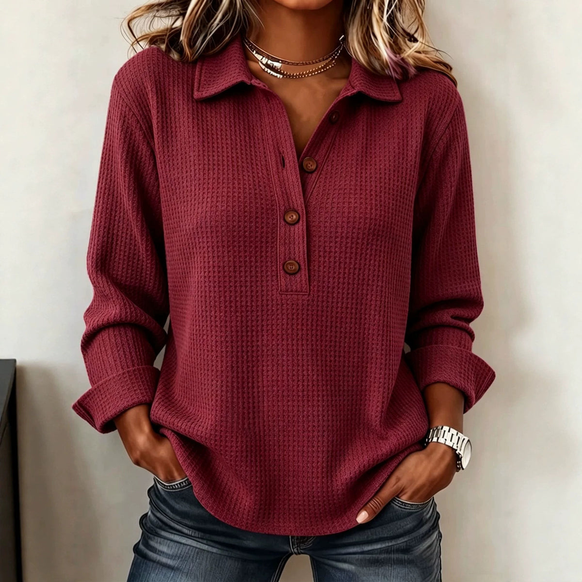 A woman wearing a long-sleeve waffle-knit polo shirt in burgundy with a three-button placket, paired with blue jeans.