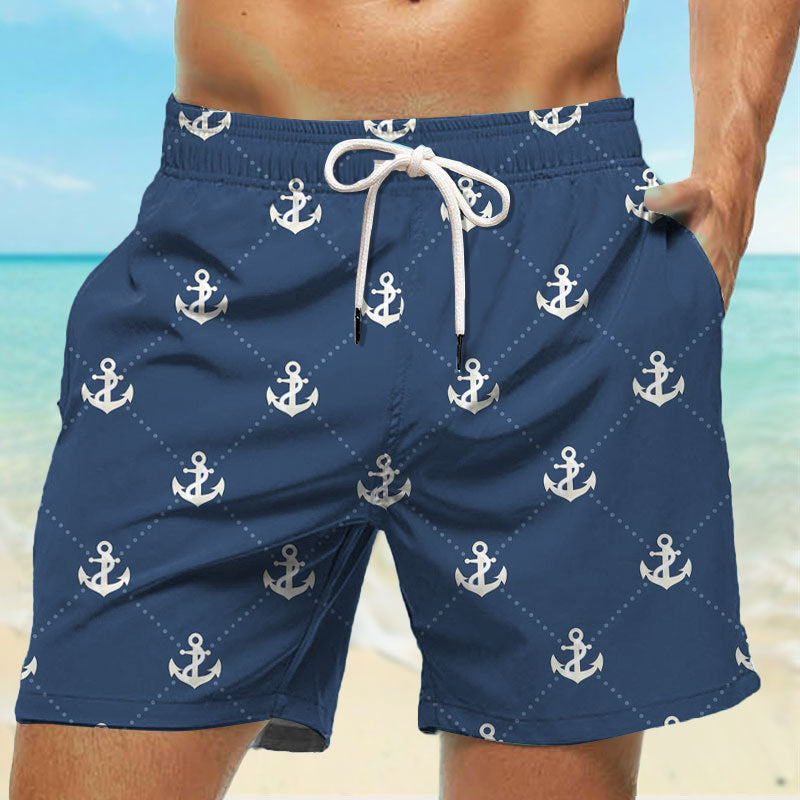 Navy blue swim shorts with white anchor pattern on a beach background