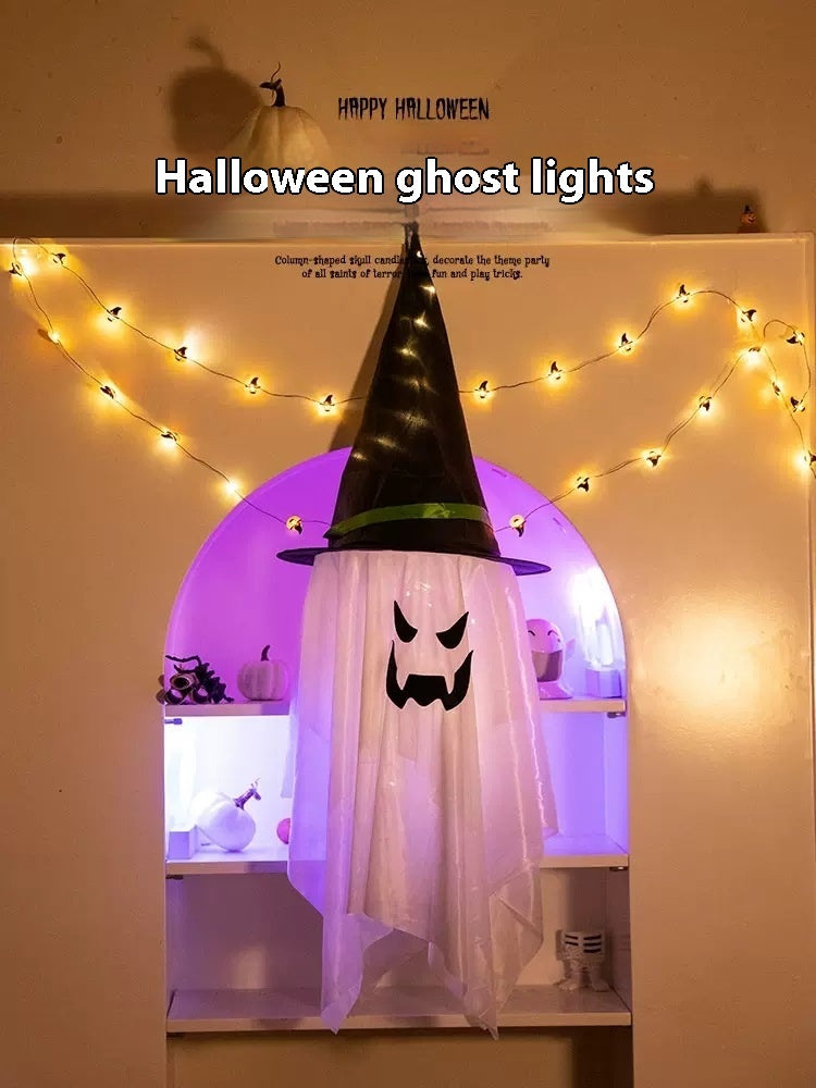 Halloween ghost decoration with a black hat and string lights on a wall.