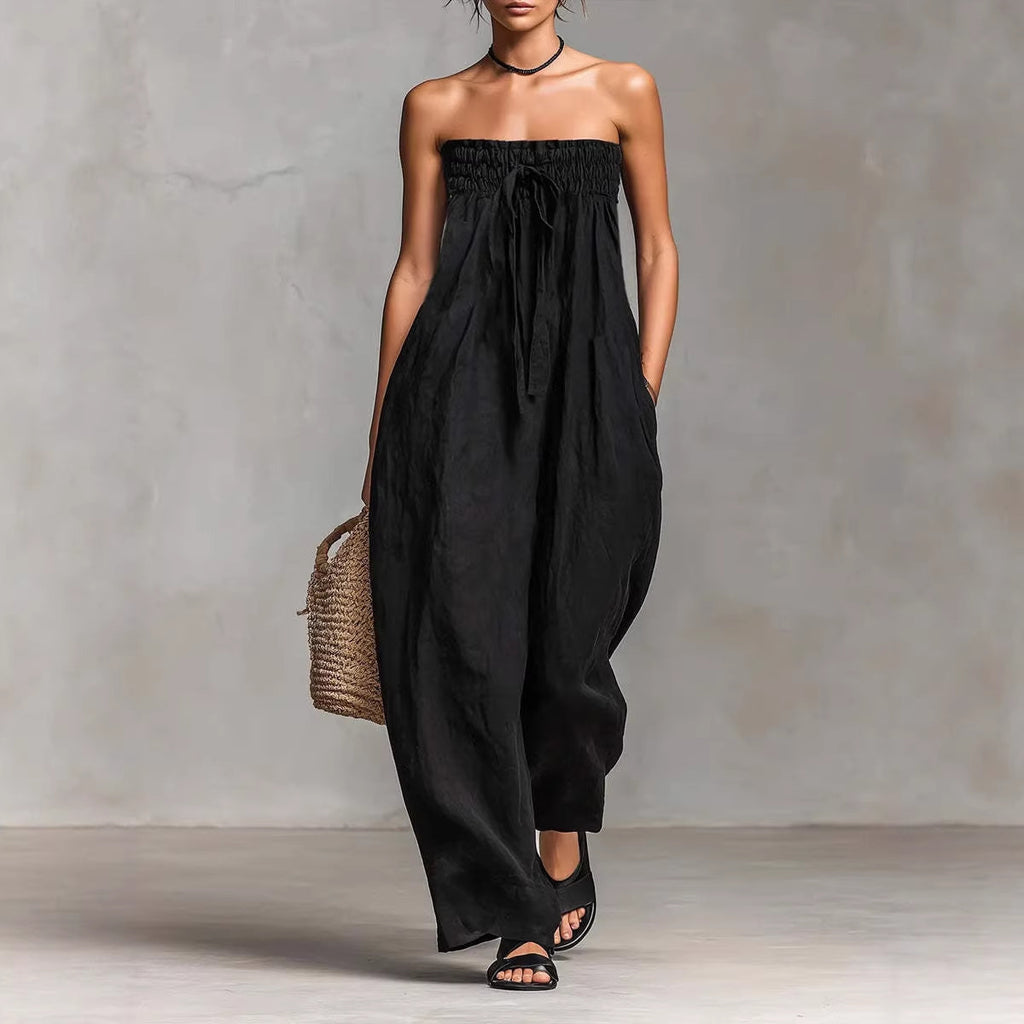 Woman wearing a black strapless jumpsuit holding a woven bag against a neutral background