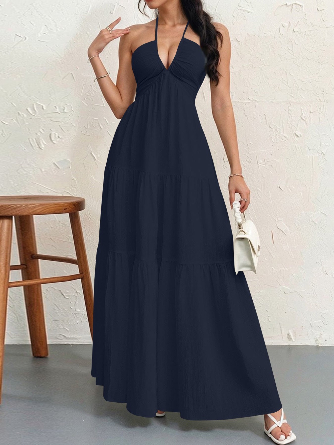Woman wearing a long navy dress against a white wall.