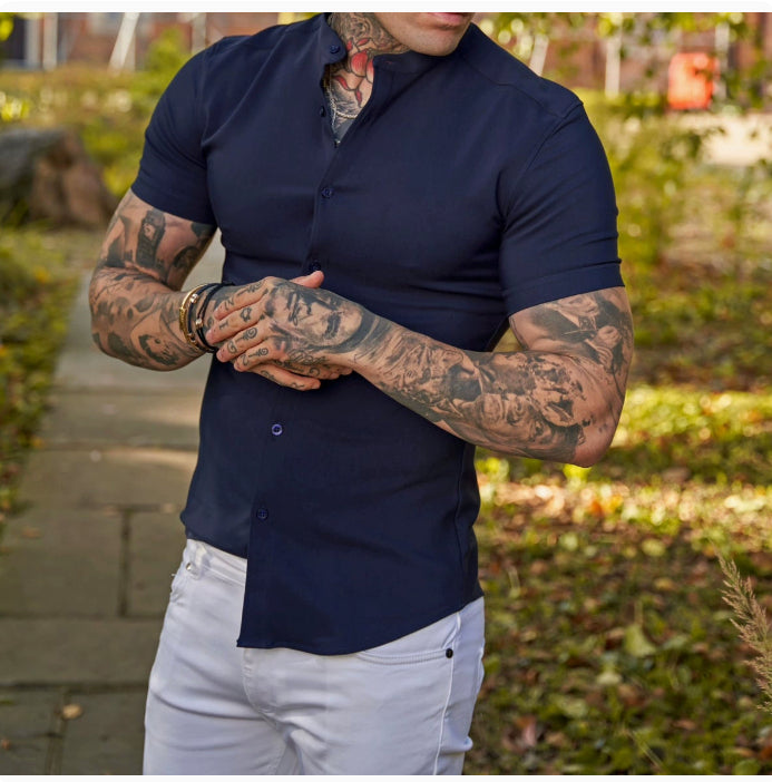 Person wearing a navy blue shirt with tattoos on arms standing outdoors.
