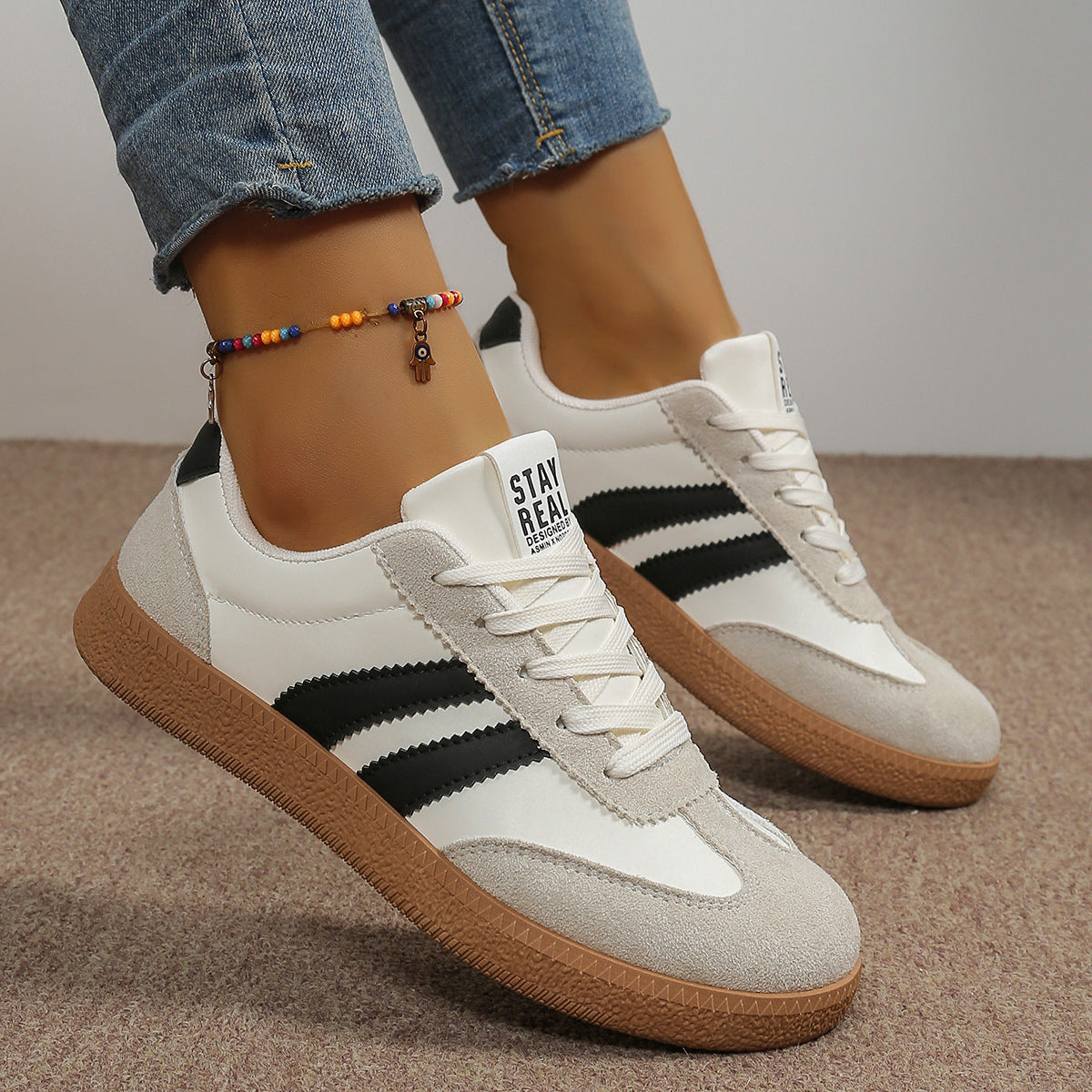 White sneakers with black stripes and brown soles worn with rolled-up jeans on a neutral background