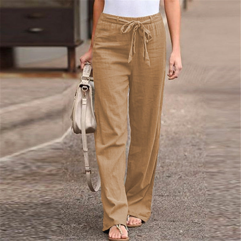 Person wearing tan pants holding a beige handbag on a street.