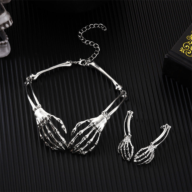 Silver skeleton hand necklace and earrings on a black textured background