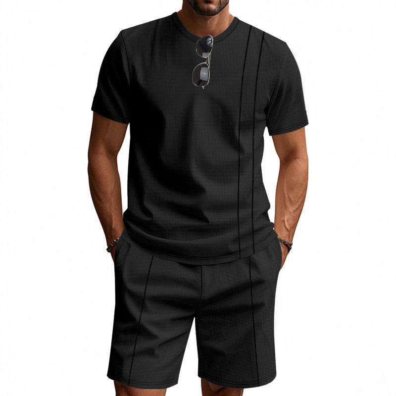 Man wearing a black t-shirt and shorts set with sunglasses on a white background