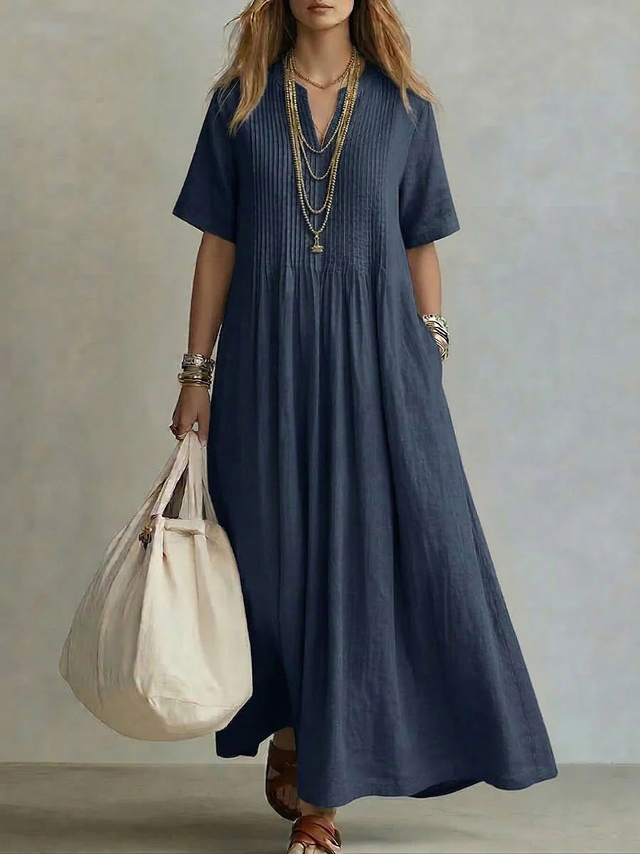 Woman wearing a long blue dress holding a beige bag against a neutral background