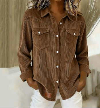 A woman wearing a brown corduroy button-up shirt with two chest pockets and white pants, shown from the shoulders to the hips in an indoor setting.