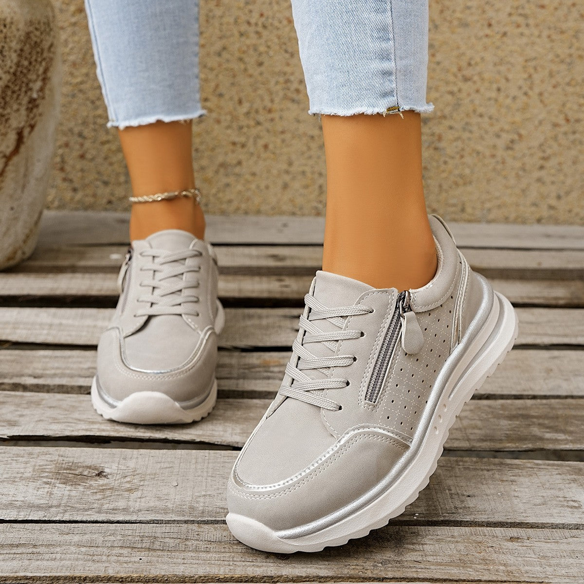 Beige sneakers worn with light blue jeans on a wooden floor.